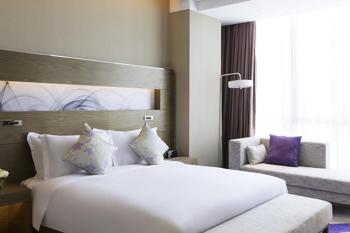A modern hotel room with a large bed, a sofa, a nightstand, and a floor lamp.
