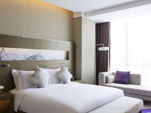 A modern hotel room with a large bed, a sofa, a nightstand, and a floor lamp.