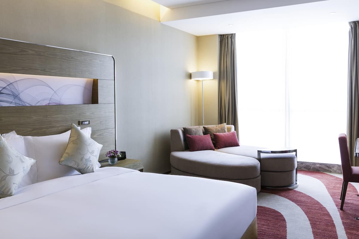 A hotel room with a large bed, a sofa, a small table, and a chair.
