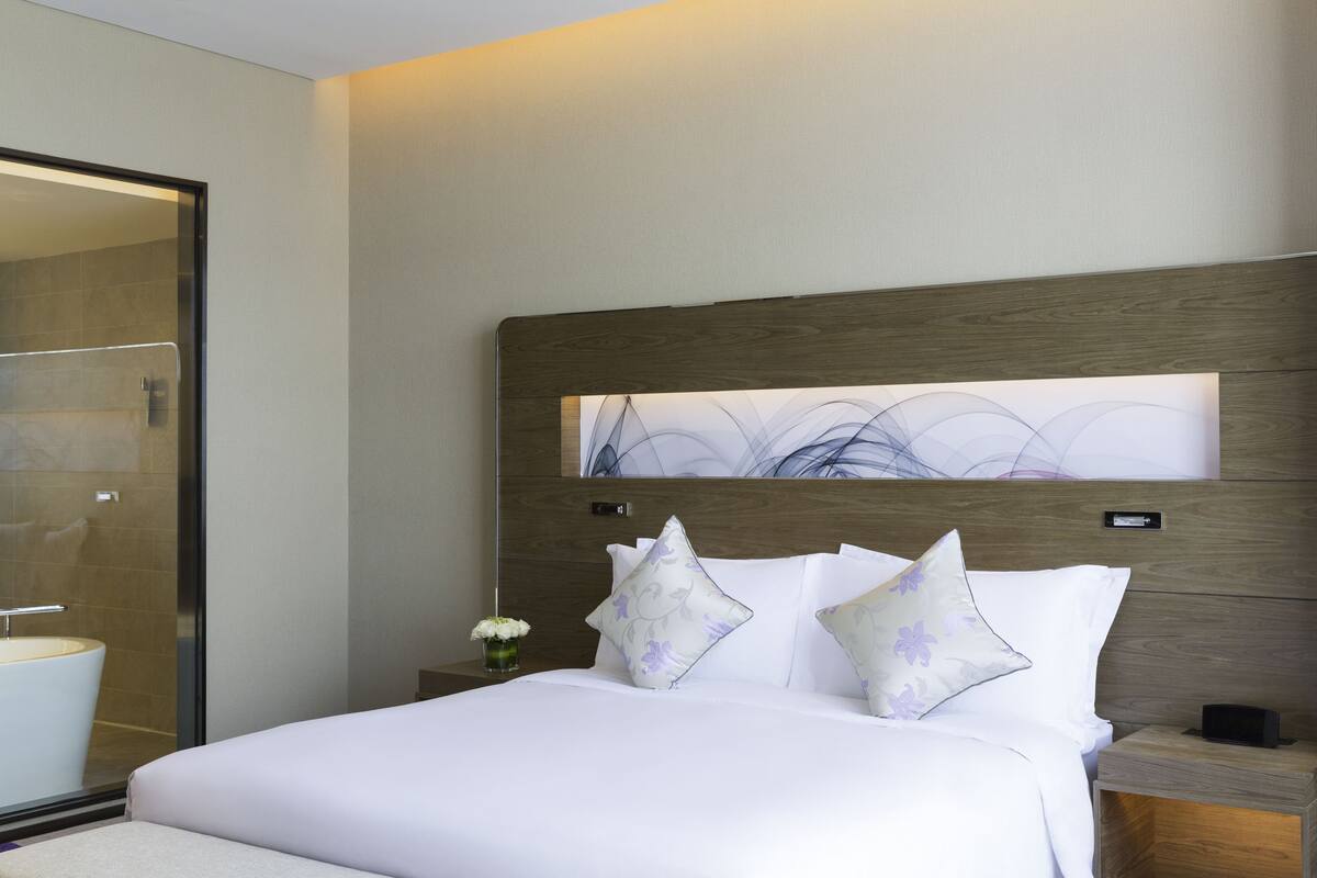A modern hotel room with a large bed, a nightstand, a bedside table, and a large mirror.