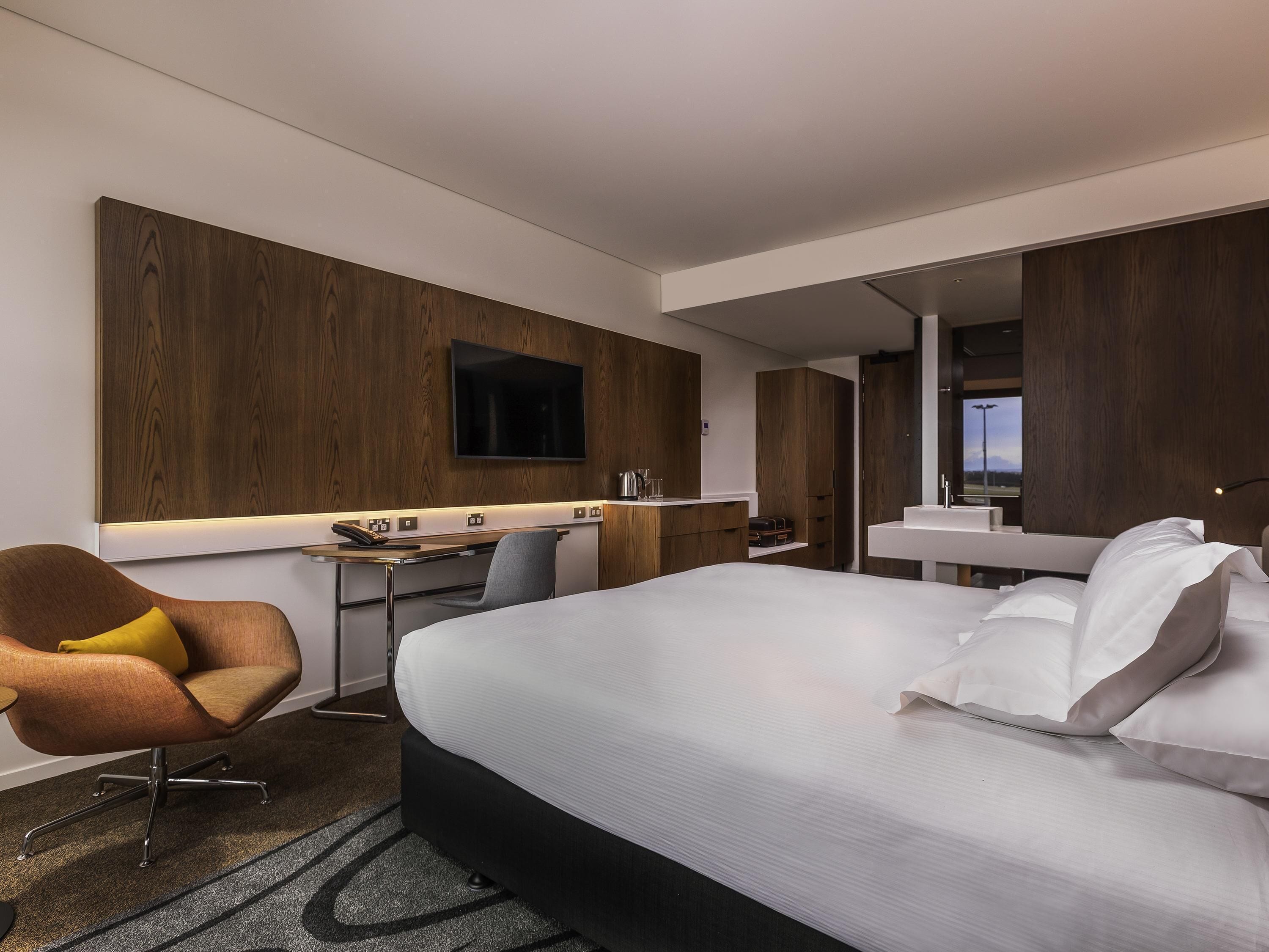 A hotel room with a bed, a desk, a chair, a TV, and a bathroom.