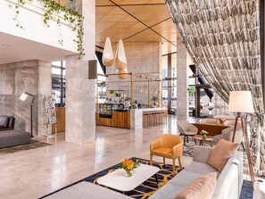 A spacious lobby with a modern bar area, seating arrangements, and a large window providing natural light. - Novotel Christchurch Airport (Christchurch)