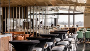A modern restaurant with high ceilings, large windows, and a variety of seating arrangements including tables and chairs.