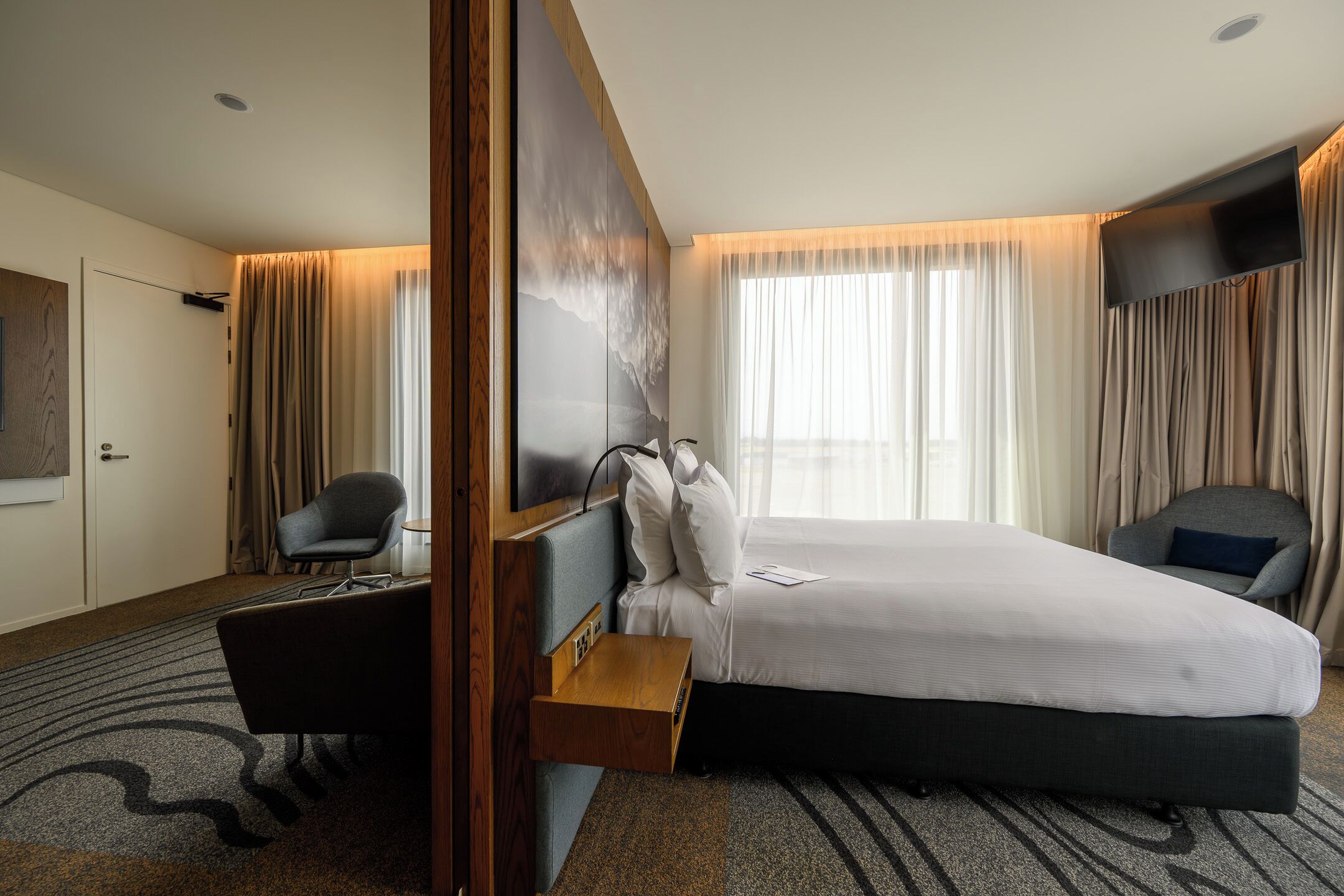 Hotelkamer met een groot bed, een bureau, een stoel, een flatscreen-tv en een groot raam met gordijnen.