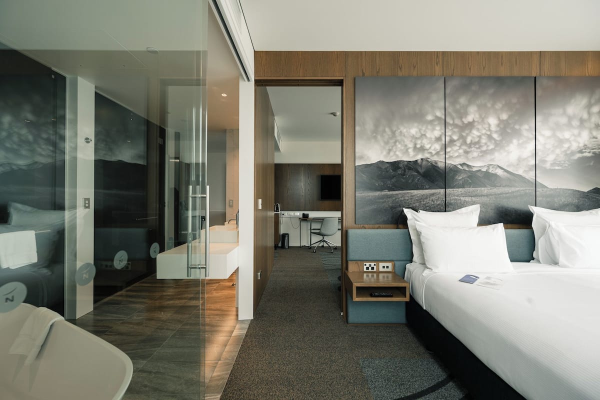 Una habitación de hotel moderna con una cama grande, un escritorio y un panel de vidrio.