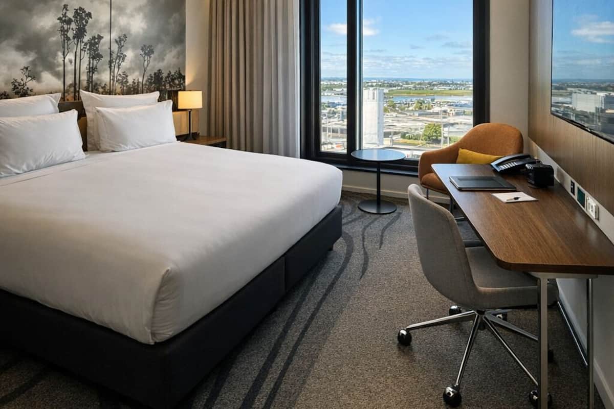 Habitación de hotel con una cama grande, un escritorio, una silla, vistas de la ciudad y un cuadro en la pared.