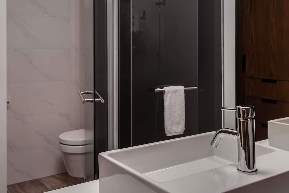 Un baño moderno con ducha envuelta en vidrio, un lavabo blanco con grifo cromado y un inodoro blanco.