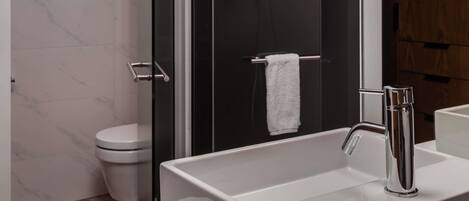A modern bathroom with a glass-enclosed shower, a white sink with a chrome faucet, and a white toilet.