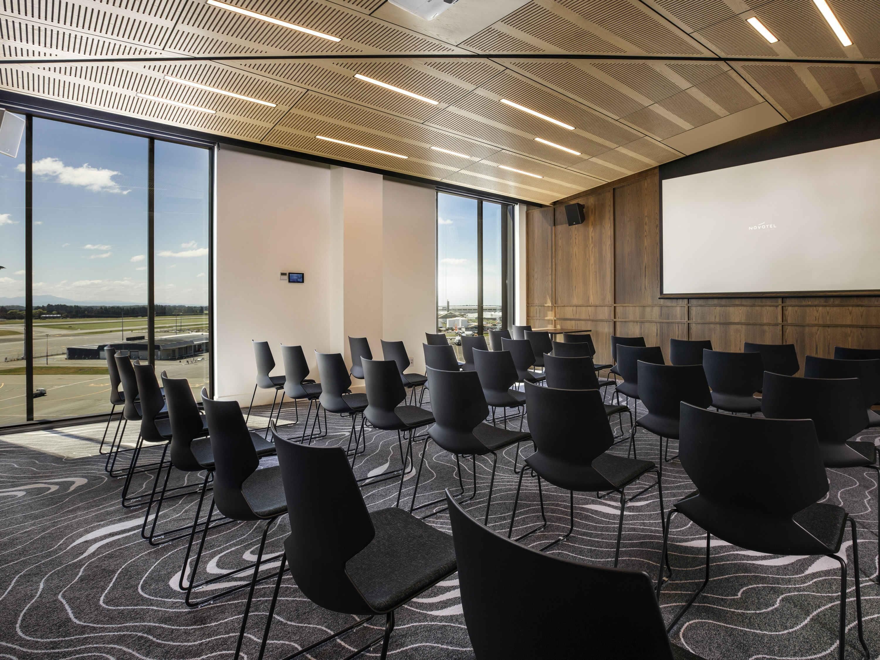 A conference room with a large screen, rows of chairs, and a view of the airport.