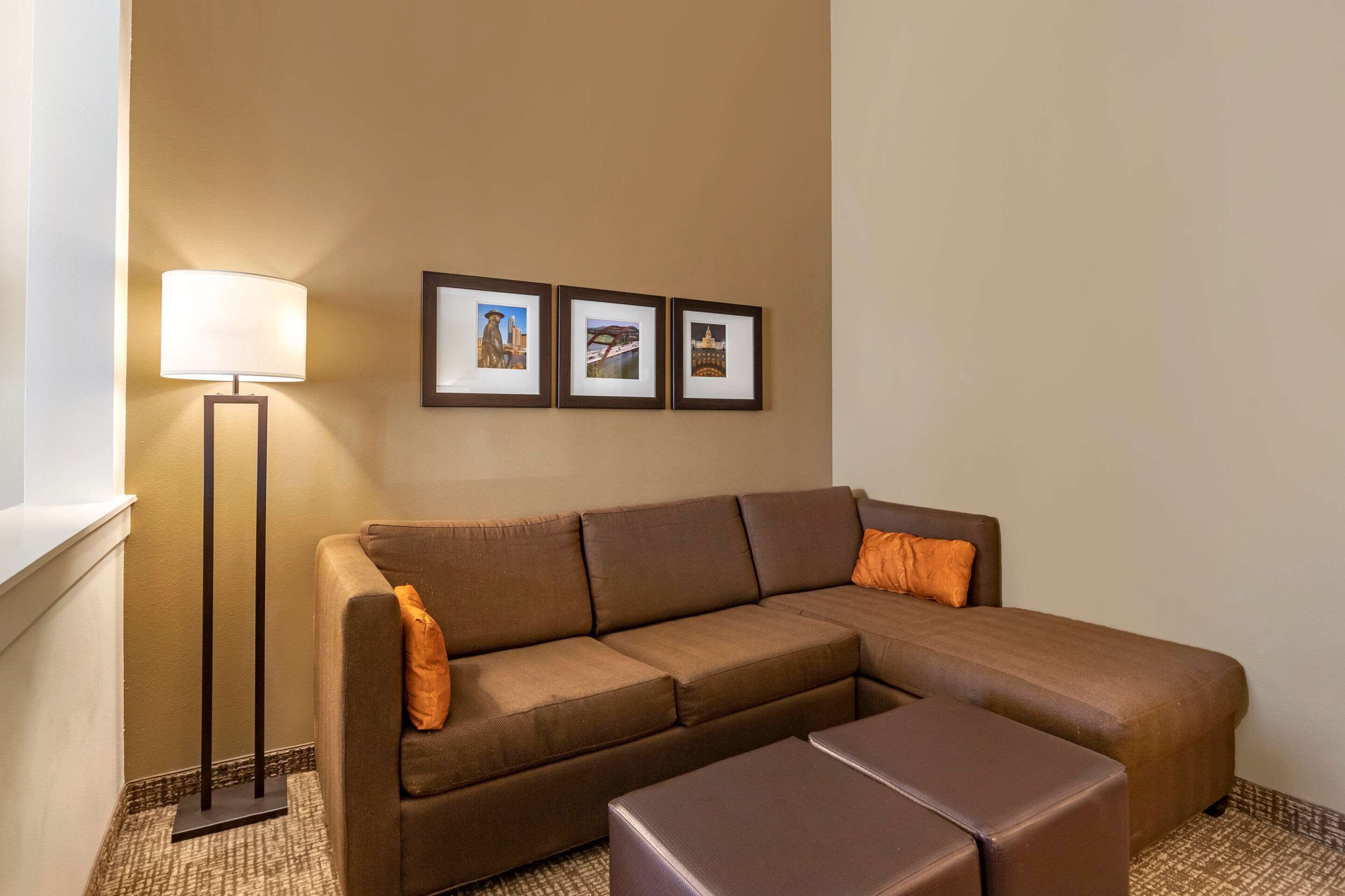 A brown sectional sofa with an ottoman, a floor lamp, and three framed pictures on the wall.