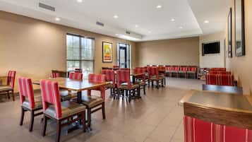 A spacious dining area with multiple tables and chairs, large windows, and a flat-screen TV mounted on the wall.