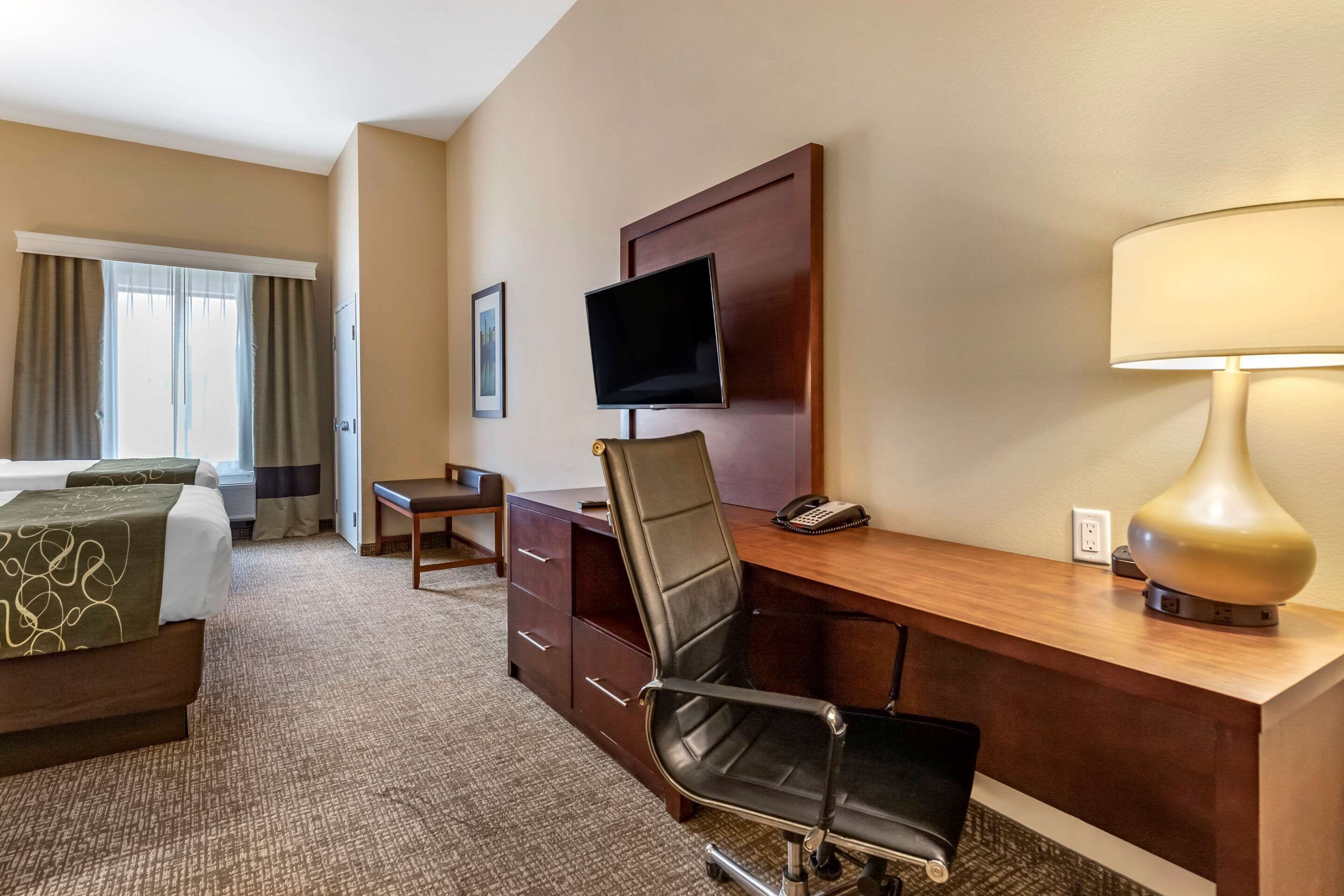 A hotel room with a bed, desk, chair, TV, lamp, and a window with curtains.