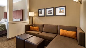A hotel room with a large L-shaped sofa, two ottomans, a bed with a headboard, and three framed pictures on the wall. - Comfort Suites Kyle (Kyle)