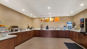 A modern hotel kitchen with a buffet setup, including a coffee machine, a refrigerator, and various food items on display. - Comfort Suites Kyle (Kyle)