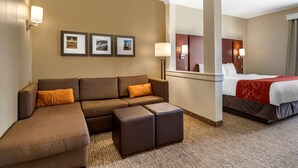 A hotel room with a sectional sofa, a bed, a small table, and a mirror. - Comfort Suites Kyle (Kyle)