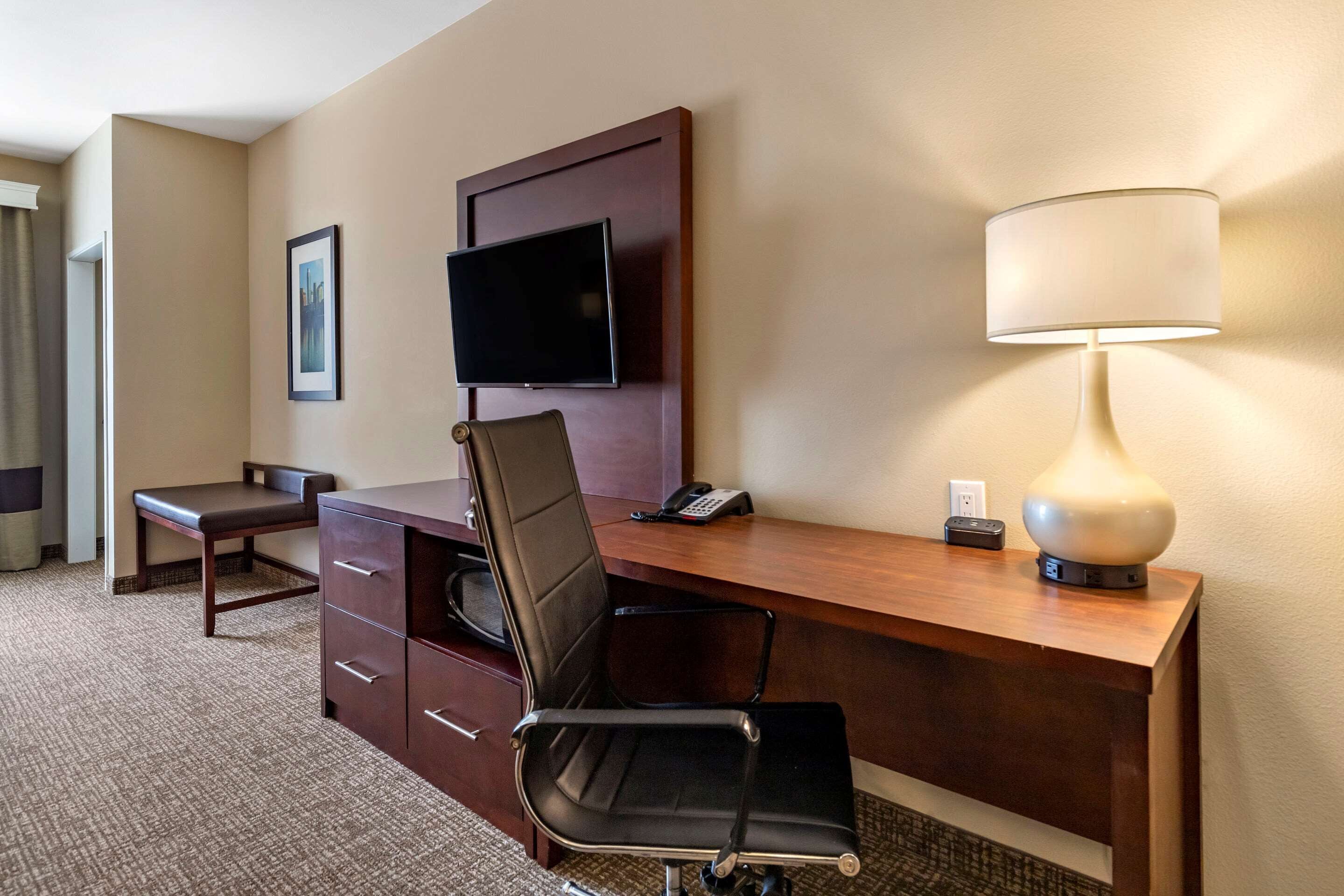 Habitación de hotel con un escritorio de madera, una silla de oficina negra, un televisor montado en la pared, una lámpara sobre el escritorio y un teléfono.