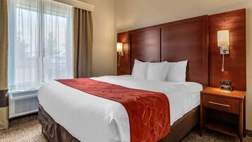A hotel room with a large bed, a wooden headboard, a bedside table with a lamp, and a window with curtains.