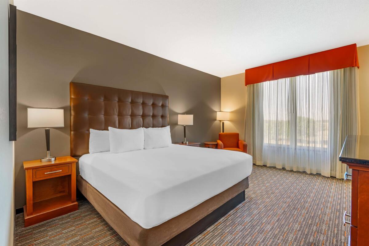 Habitación de hotel con una cama grande, dos mesitas de noche, una silla, un escritorio y una ventana con cortinas.