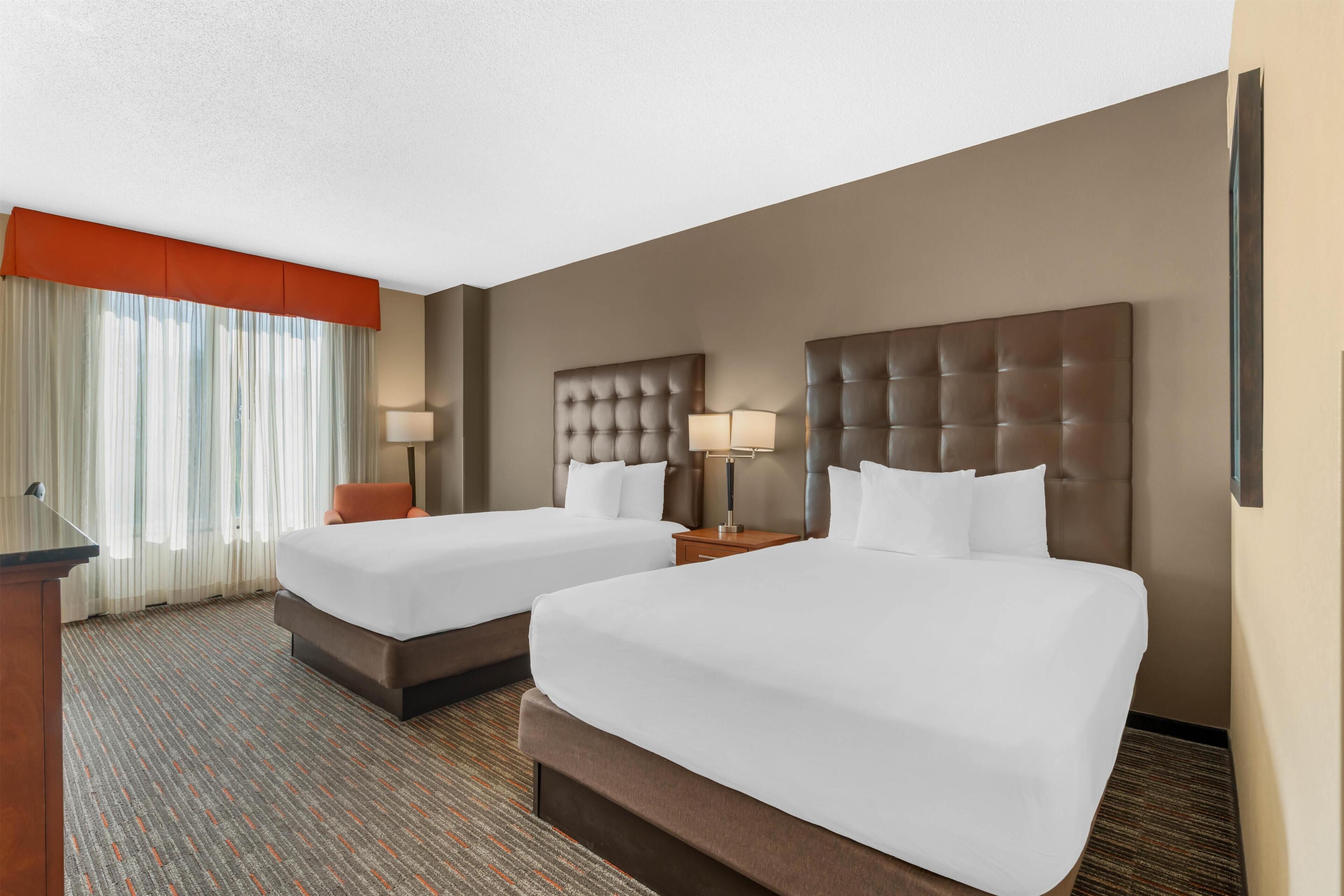 A hotel room with two beds, a desk, and a window with curtains.