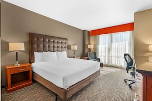 Une chambre d’hôtel avec un grand lit, deux tables de chevet avec des lampes, un bureau avec une chaise et une fenêtre avec des rideaux.