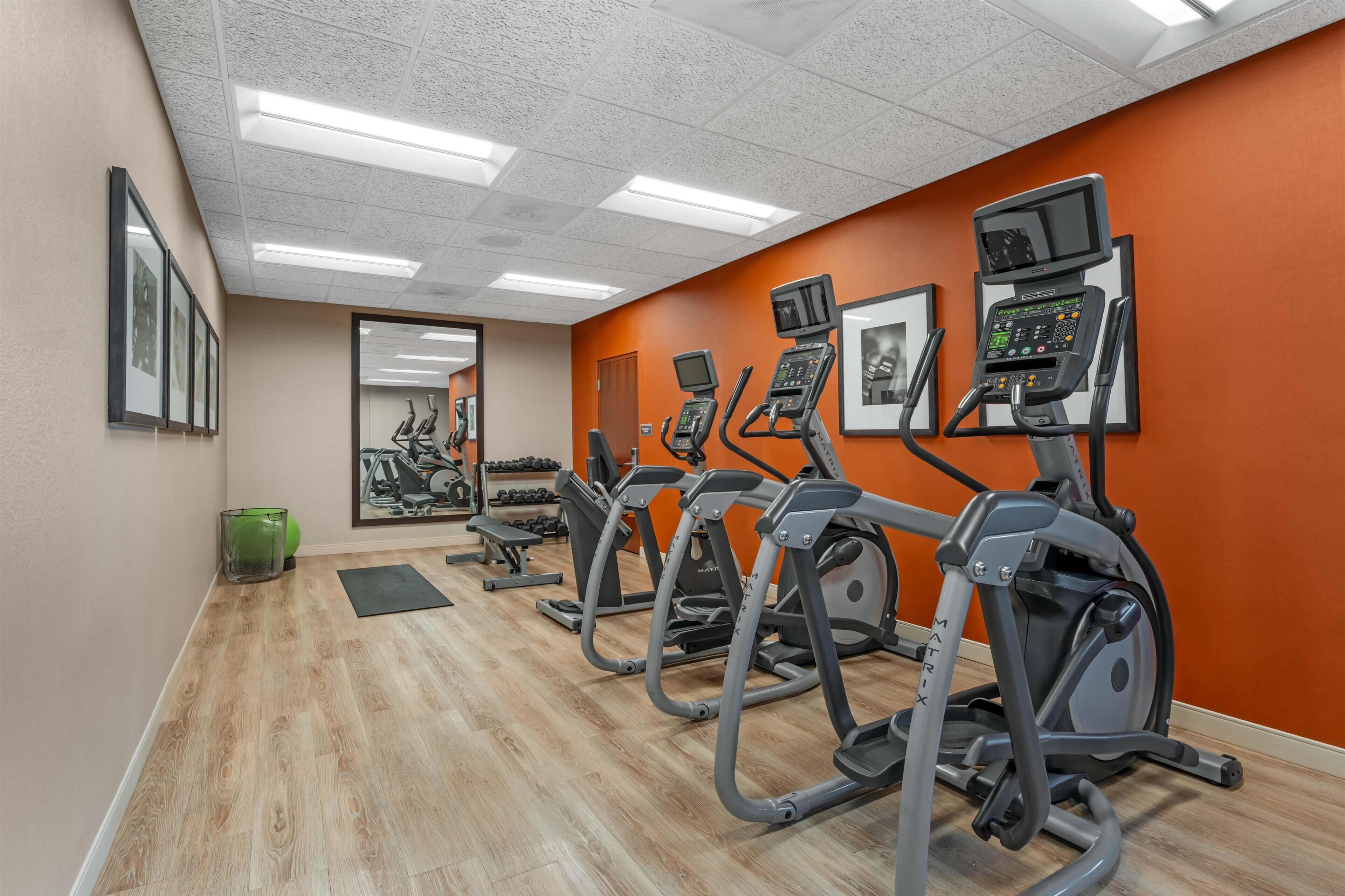 Un gimnasio con cintas de correr, un espejo grande y suelo de madera.