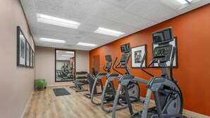 Een fitnessruimte met loopbanden, een spiegelwand en een houten vloer.