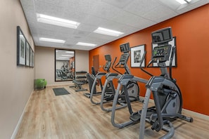 Une salle de sport équipée de tapis de course, dotée d’un mur recouvert de miroirs et d’un plancher en bois.
