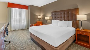 Habitación de hotel con una cama grande, dos lámparas de noche, un sillón naranja, un escritorio con silla y una ventana con cortinas traslúcidas.