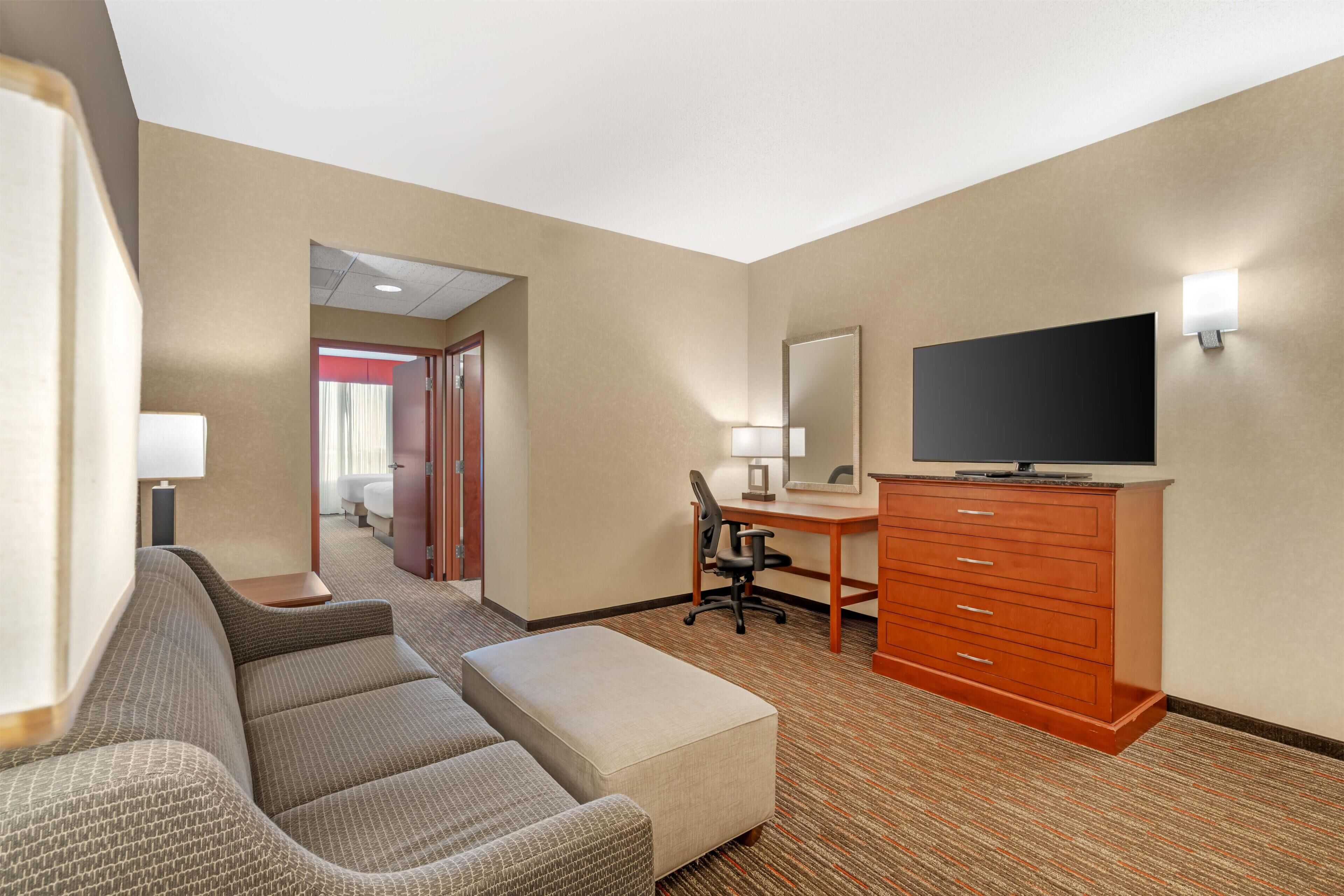 Habitación de hotel con sofá, escritorio, televisión y baño visible a través de una puerta abierta.