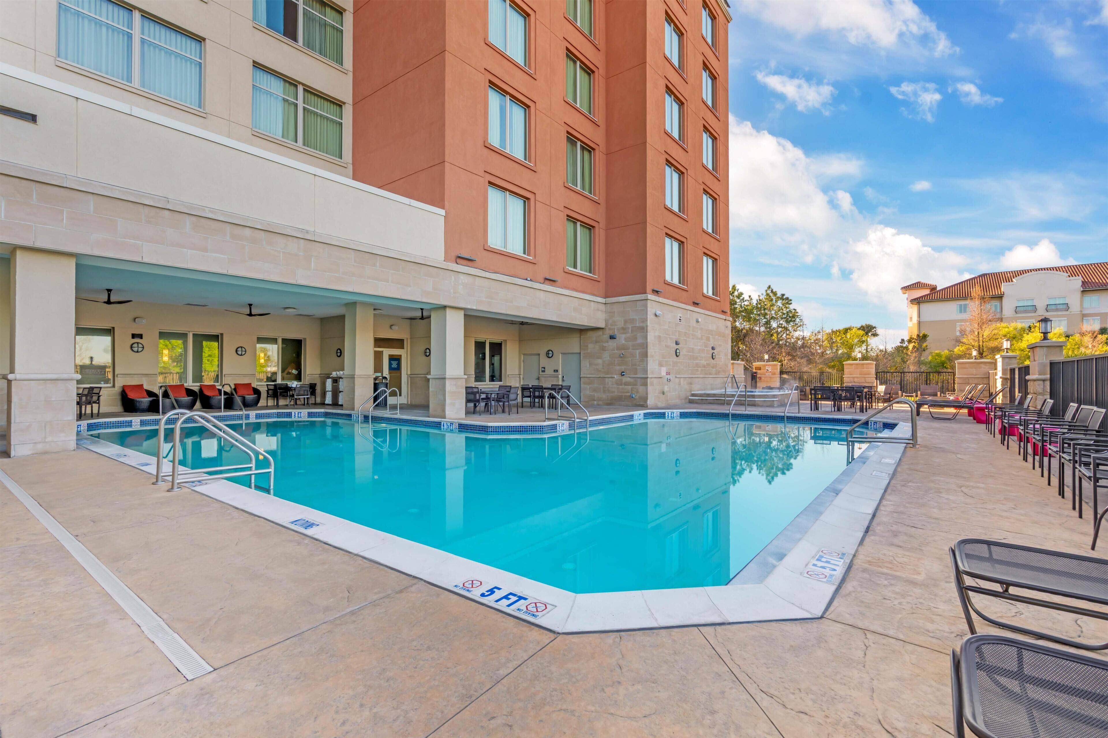 A hotel pool area with a clear blue pool, lounge chairs, and a covered seating area.
