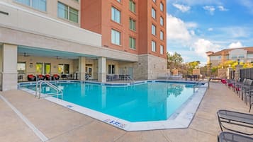 A hotel pool area with a clear blue pool, lounge chairs, and a covered seating area.