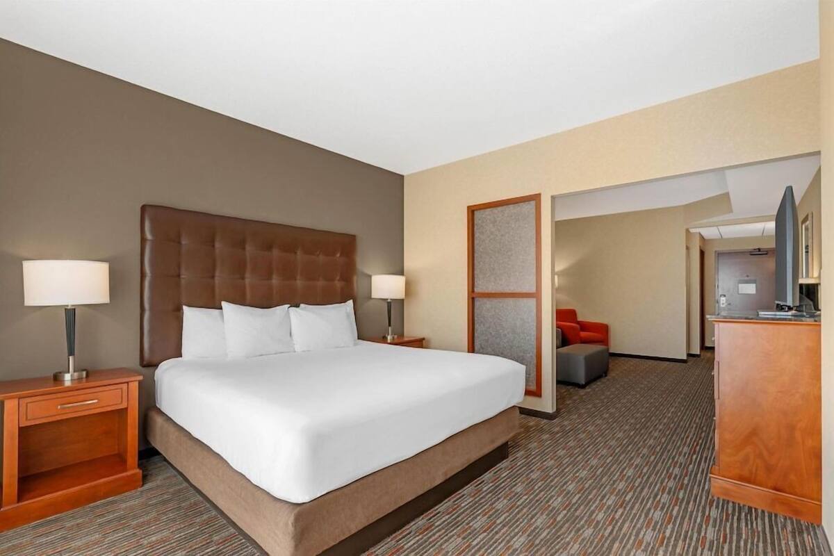 Une chambre d’hôtel avec un grand lit, une table de chevet en bois, un bureau avec une lampe, une télévision et un fauteuil rouge.
