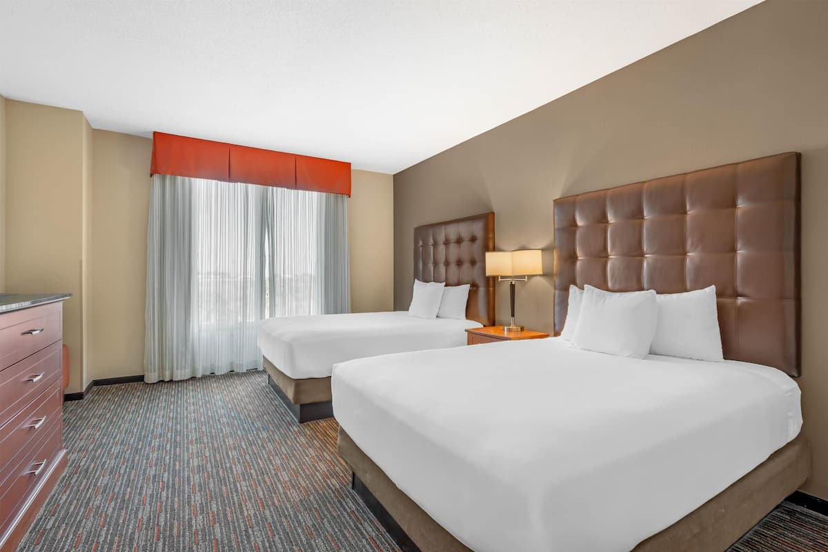 Une chambre d’hôtel avec deux lits, une commode, une fenêtre avec des rideaux et une lampe.