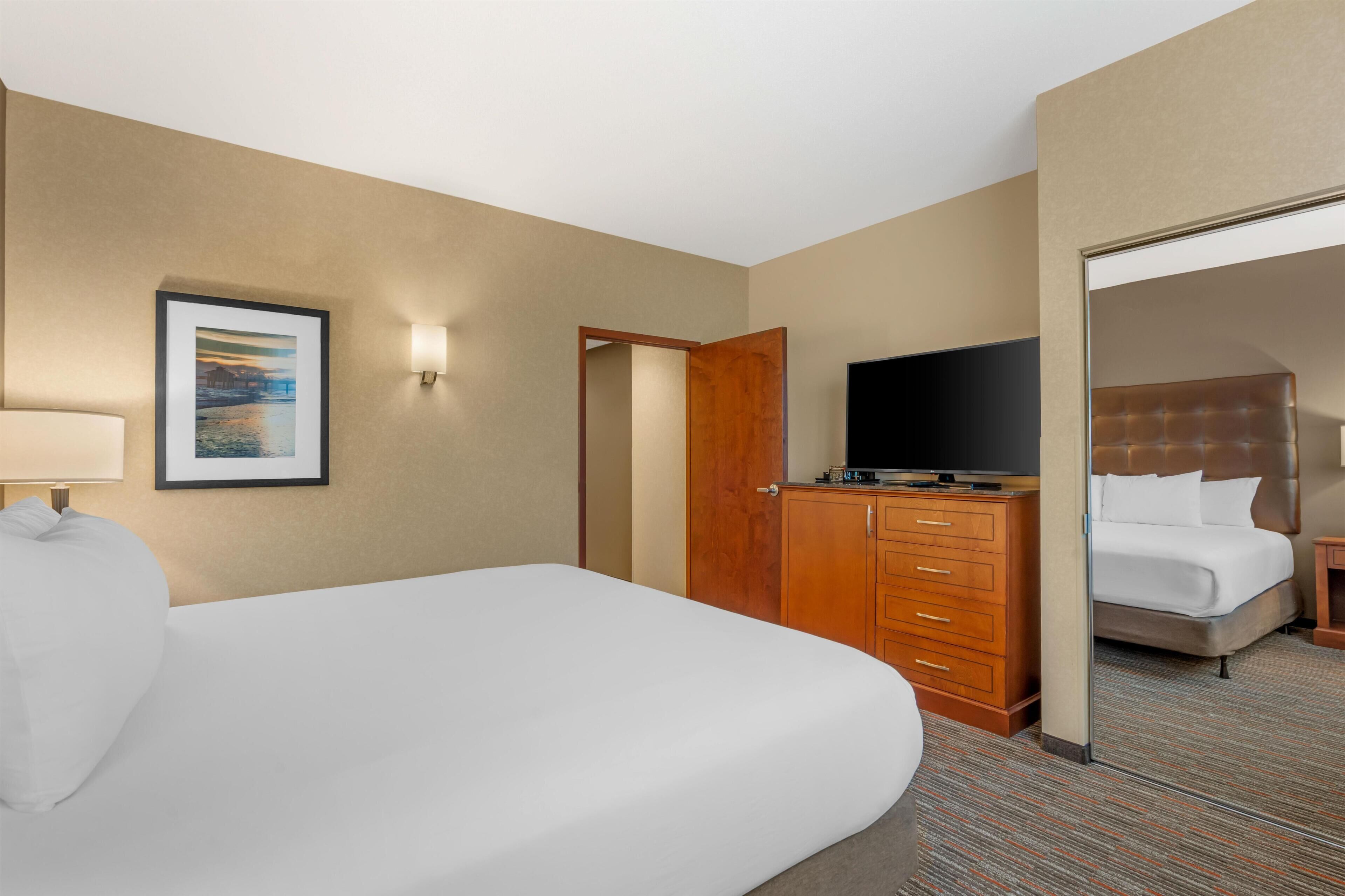A hotel room with a bed, a television, a dresser, and a door leading to another room.