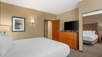 A hotel room with a bed, a television, a dresser, and a door leading to another room.