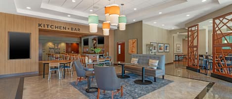 A modern hotel lobby with a kitchen and bar area, seating arrangements, and a decorative ceiling.
