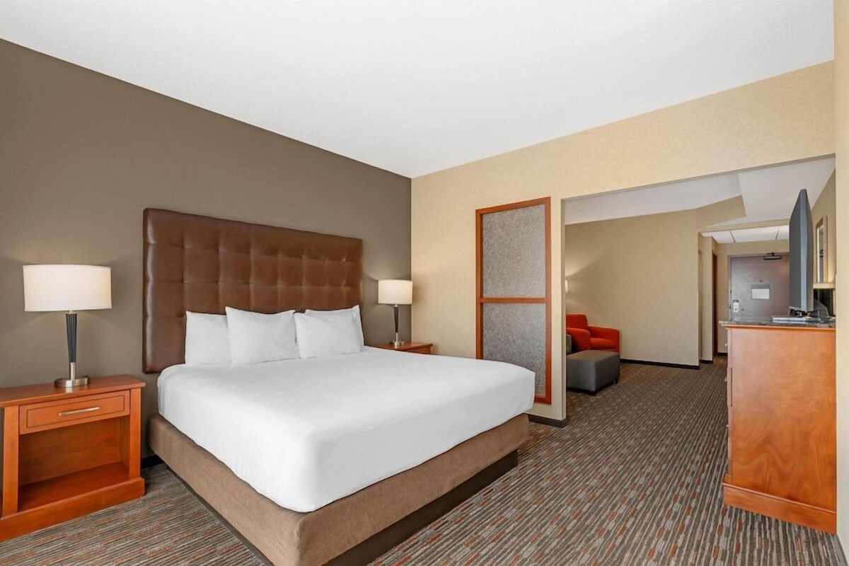Een hotelkamer met een groot bed, een houten nachtkastje, een bureau met lamp, een televisie en een rode stoel.