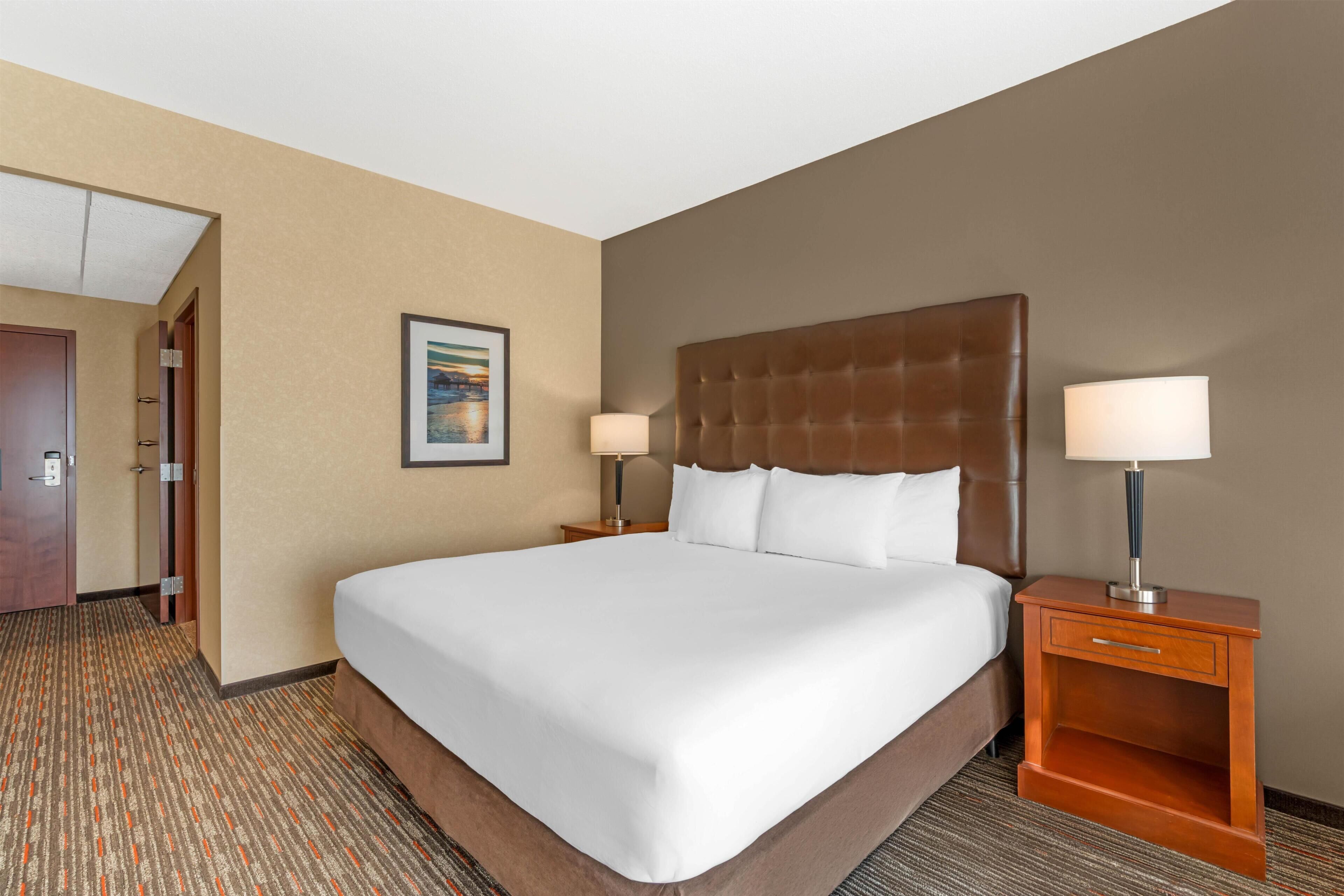 A hotel room with a large bed, two bedside tables with lamps, a door, and a carpeted floor.