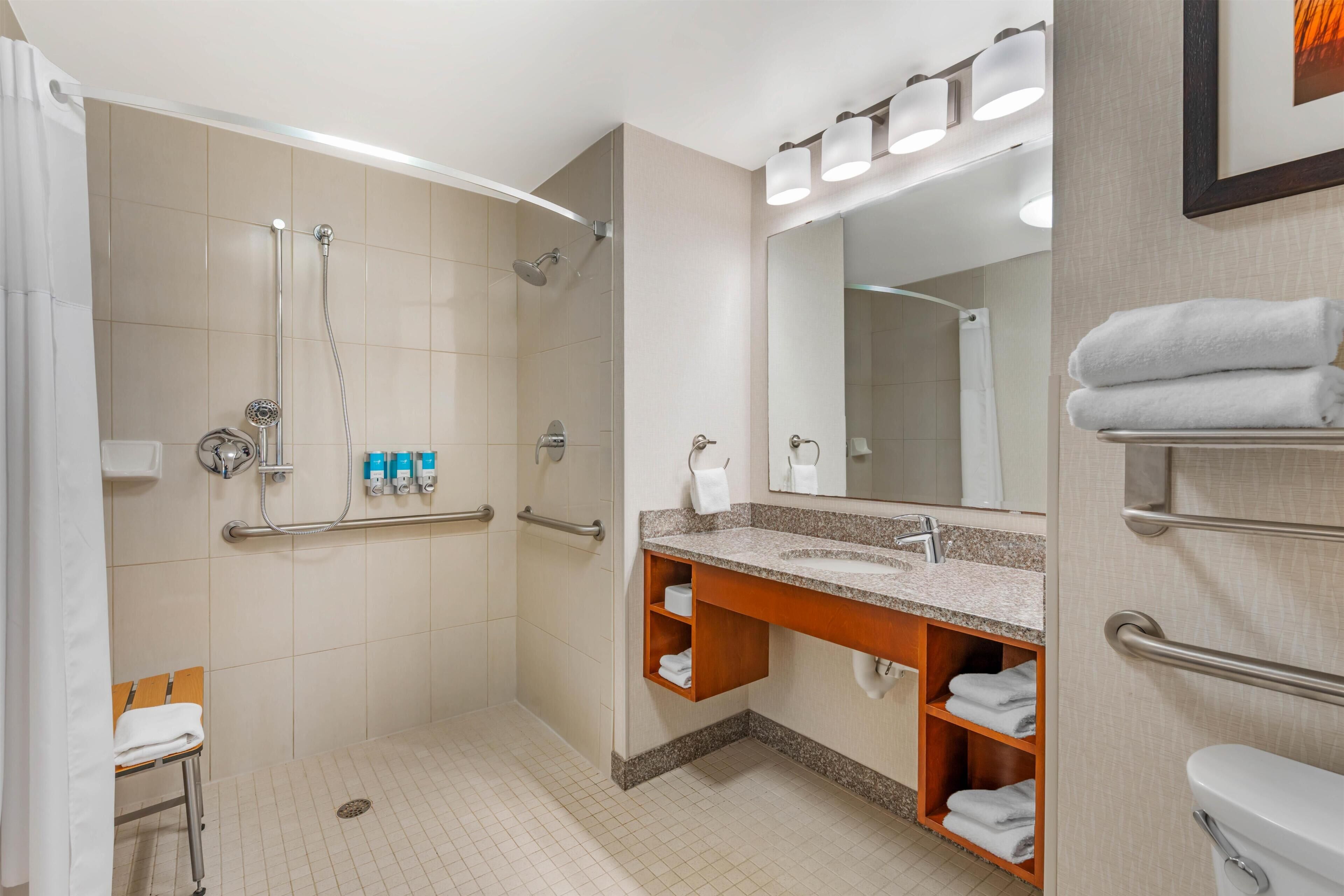 A modern bathroom with a shower, toilet, and sink, equipped with grab bars and a hand dryer.