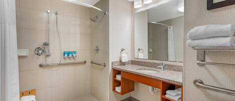 Une salle de bain moderne équipée d’une douche, de toilettes et d’un lavabo, ainsi que de barres d’appui et d’un sèche-mains.