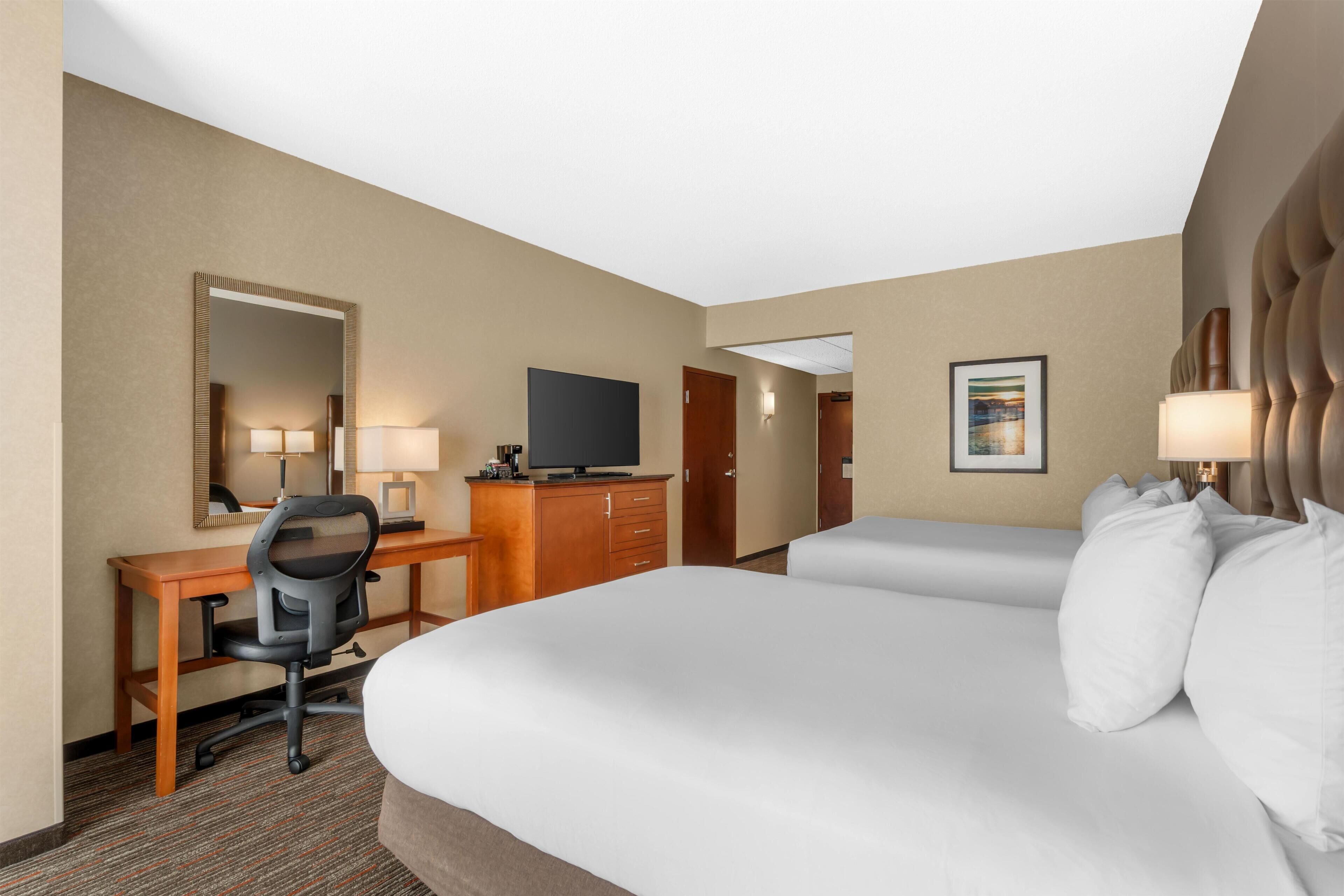 Una habitación de hotel con cama, escritorio, silla, televisión y puerta.
