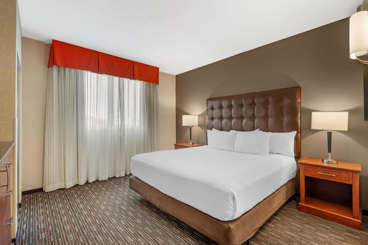 Une chambre d’hôtel avec un grand lit, deux tables de chevet avec des lampes, un rideau rouge et une moquette à rayures.