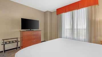A hotel room with a bed, a TV on a dresser, a window with curtains, and a small table.
