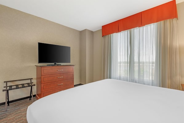 Una habitación de hotel con una cama, un televisor en una cómoda, una ventana con cortinas y una mesita.