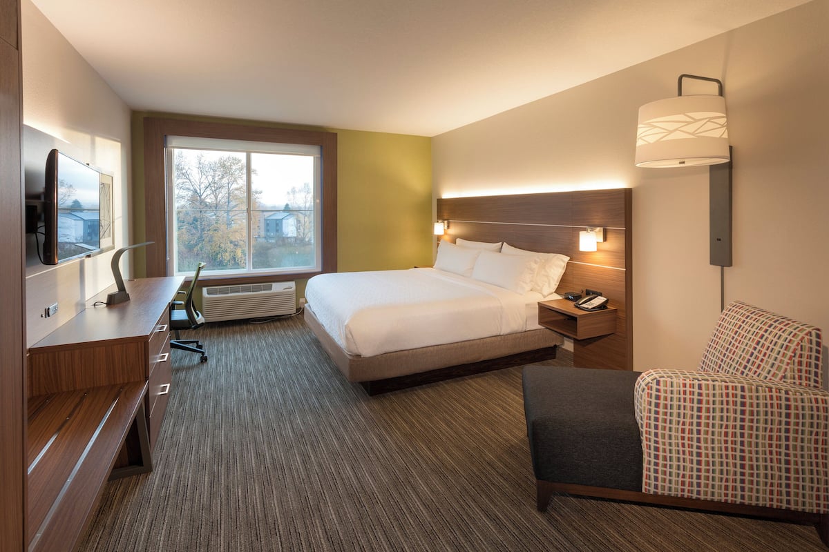 A hotel room with a large bed, bedside table, chair, desk, and a TV.