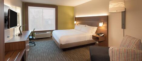 A hotel room with a bed, bedside table, lamp, chair, and a television.