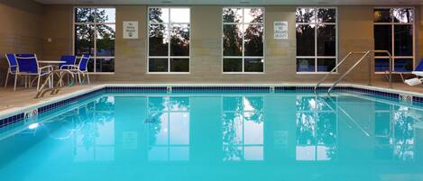 An indoor swimming pool with clear water, a diving board, and lounge chairs.