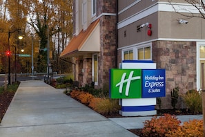 A Holiday Inn Express & Suites building with a stone facade, a green and blue sign, and a sidewalk leading to the entrance. - Holiday Inn Express & Suites Seattle South - Tukwila by IHG (Tukwila)