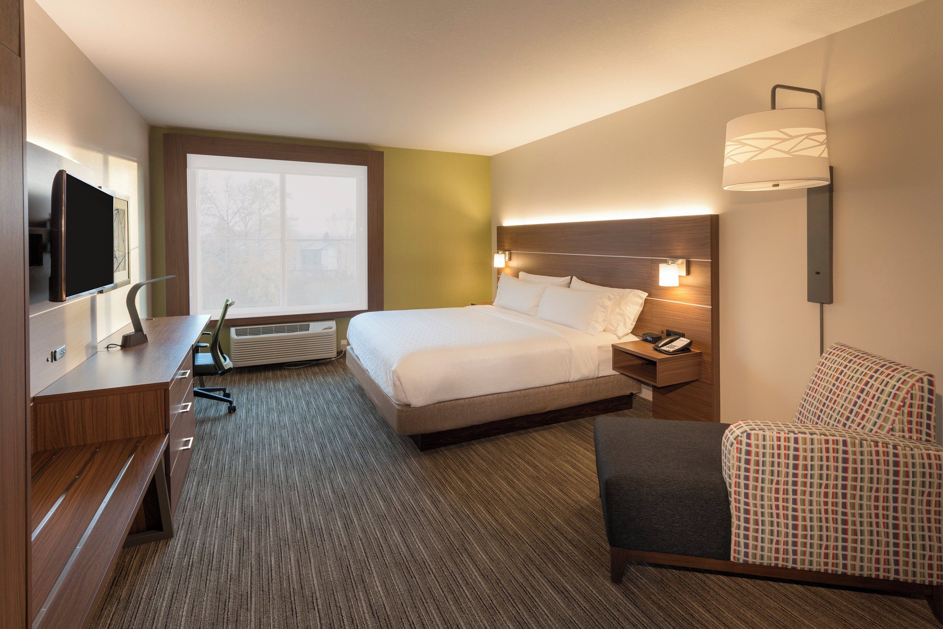 A hotel room with a bed, bedside table, chair, TV, and a window with a view.
