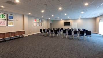 A conference room with a carpeted floor, a row of chairs, a wooden cabinet, and framed artwork on the wall.